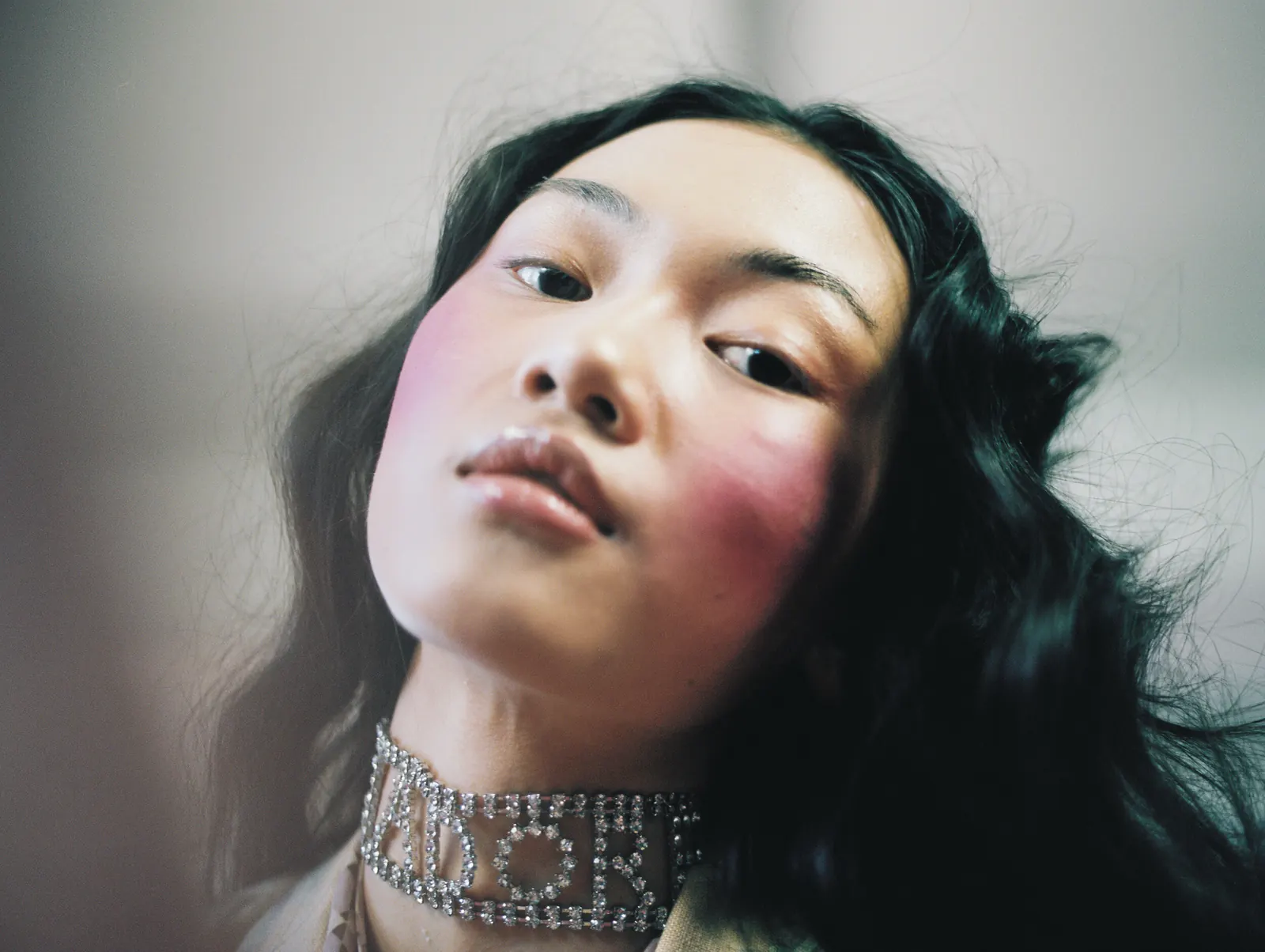 Portrait of a woman with dark wavy hair, rosy cheeks and a silver choker, shot on film