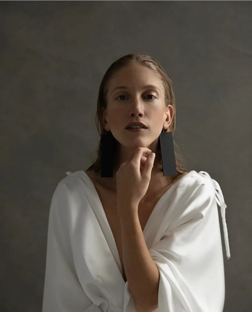 Woman with a sleek low ponytail and soft, natural makeup in a white draped top